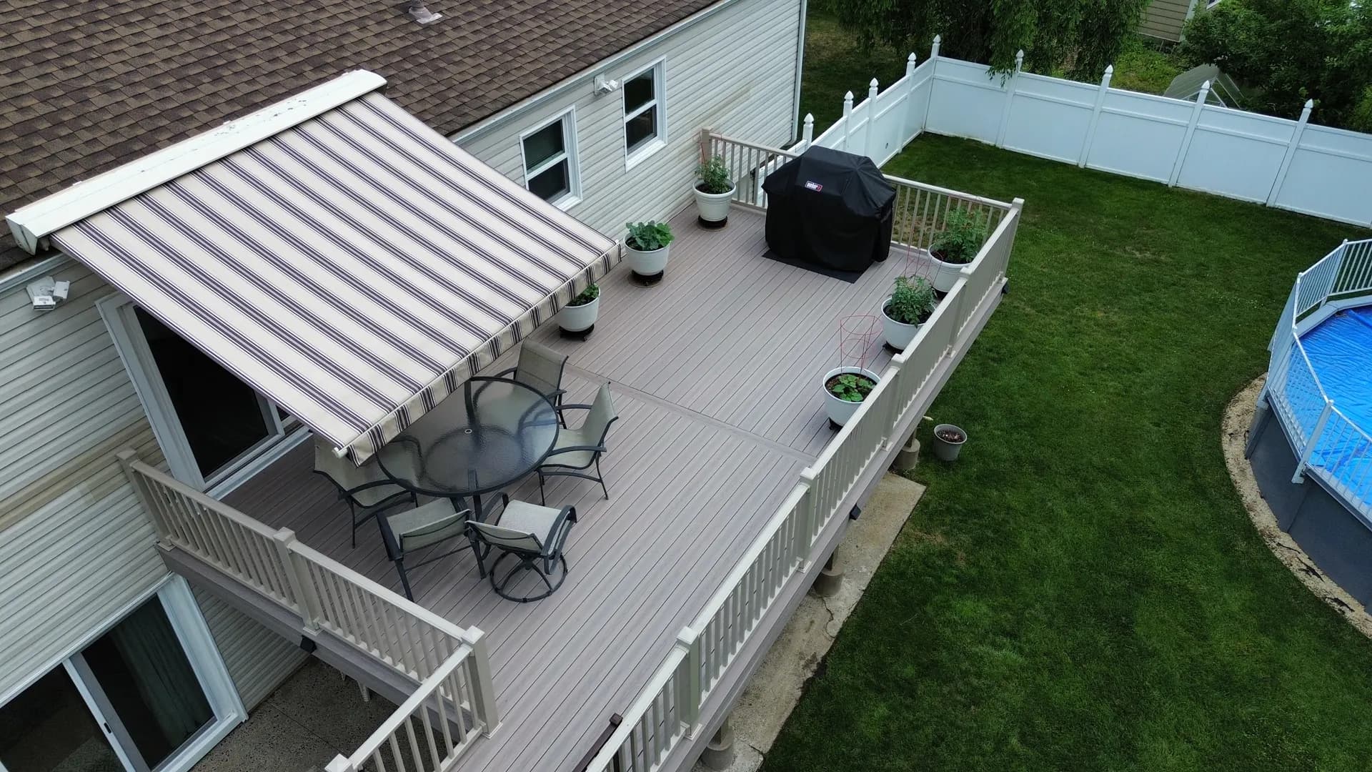 Finished composite deck with retractable awning, dining set and white aluminum railings built by Father & Sons in NJ